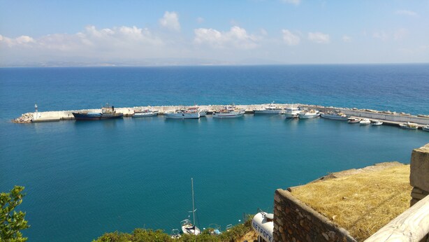 Un port de plaisance situé sur la côte, avec de nombreux bateaux amarrés, une jetée en pierre et une vue dégagée sur la mer.