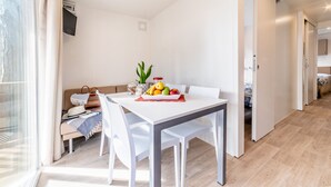 Una habitación moderna y luminosa, con una mesa de comedor preparada para dos personas, un sofá y una pequeña planta.