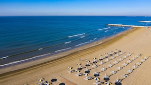 A beach with rows of sun loungers and umbrellas, a rocky breakwater, and calm blue waters. - Camping Village Cavallino (Cavallino-Treporti)