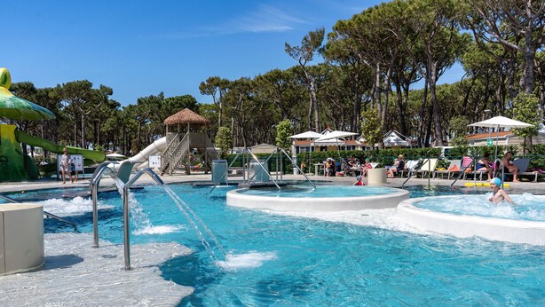 Un área de piscina con varias fuentes de agua, incluyendo un tobogán y una cascada pequeña.