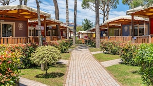 A pathway leading to a row of wooden cabins with numbered doors, surrounded by well-maintained greenery and trees. - Camping Village Cavallino (Cavallino-Treporti)