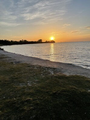 A sunset over a calm body of water with a grassy shoreline. - Charming Vacation Home in Zeeland - Park de Kreek I, Fully Renovated & Wi-Fi (Bruinisse)