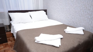 A neatly made bed with white and brown linens, a wooden nightstand, and a patterned wall. - Olimpo Guest House (Akhaltsikhe)
