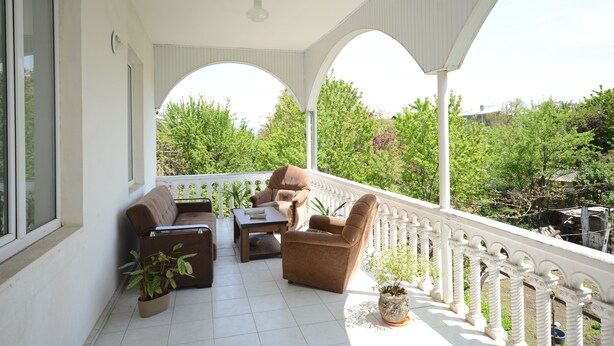 A covered outdoor seating area with a white railing, a sofa, a chair, and a table. - Olimpo Guest House (Akhaltsikhe)