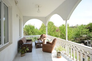 Een overdekt buitengebied met een witte balustrade, een bank, een stoel en een tafel.