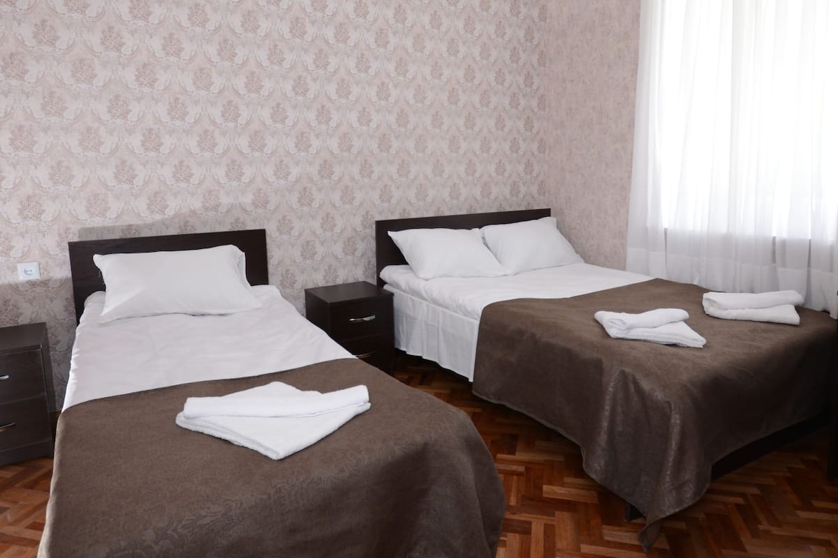 A hotel room with two beds, wooden parquet flooring, and a patterned wallpaper.