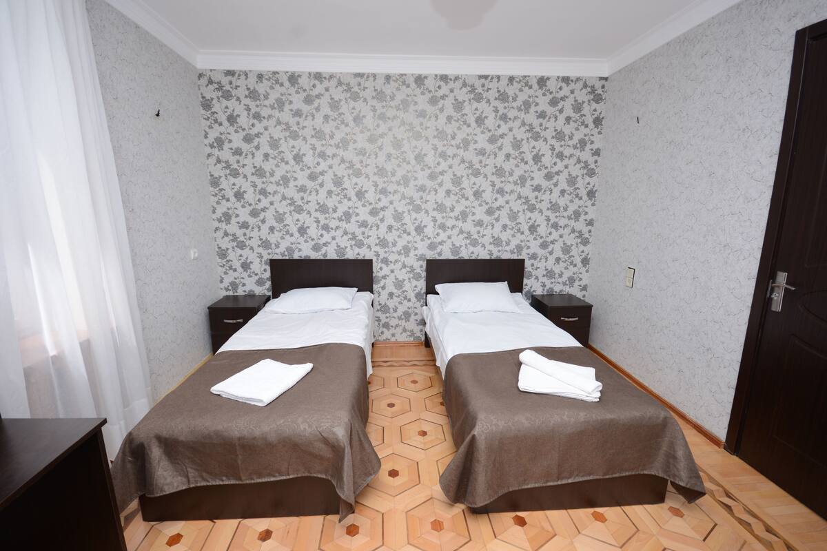 A double room with two beds, a wooden floor, and floral wallpaper.