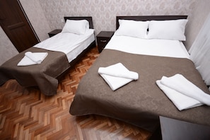 A hotel room with two beds, each with a brown bedspread and white pillows. There are folded towels on each bed. The room has a wooden herringbone floor and a door visible in the background. - Olimpo Guest House (Akhaltsikhe)