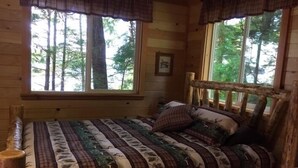 Une chambre confortable dans un chalet, avec un lit en bois, une literie à carreaux et de grandes fenêtres donnant sur la forêt.