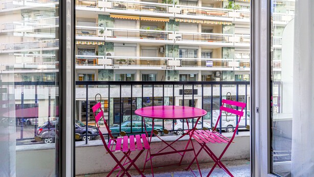 Ein Balkon mit rotem Tisch und Stühlen, Blick auf ein Mehrfamilienhaus mit Balkonen und ein Fliesenboden.