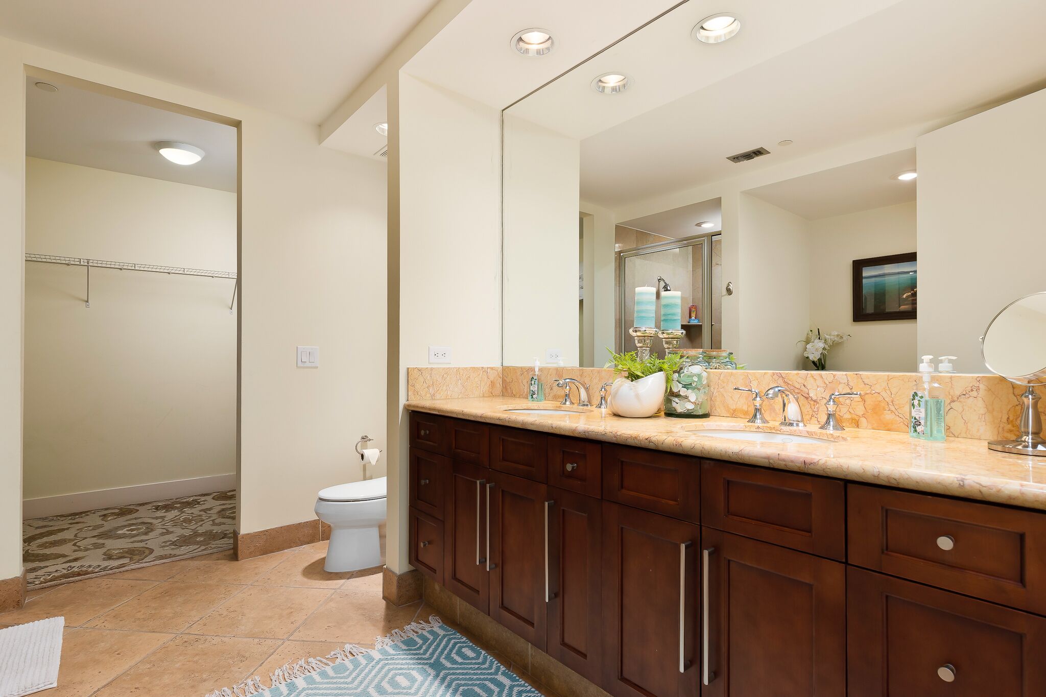 A modern bathroom with a large mirror, dark wooden cabinets, a marble countertop, and a shower area visible through an open door.