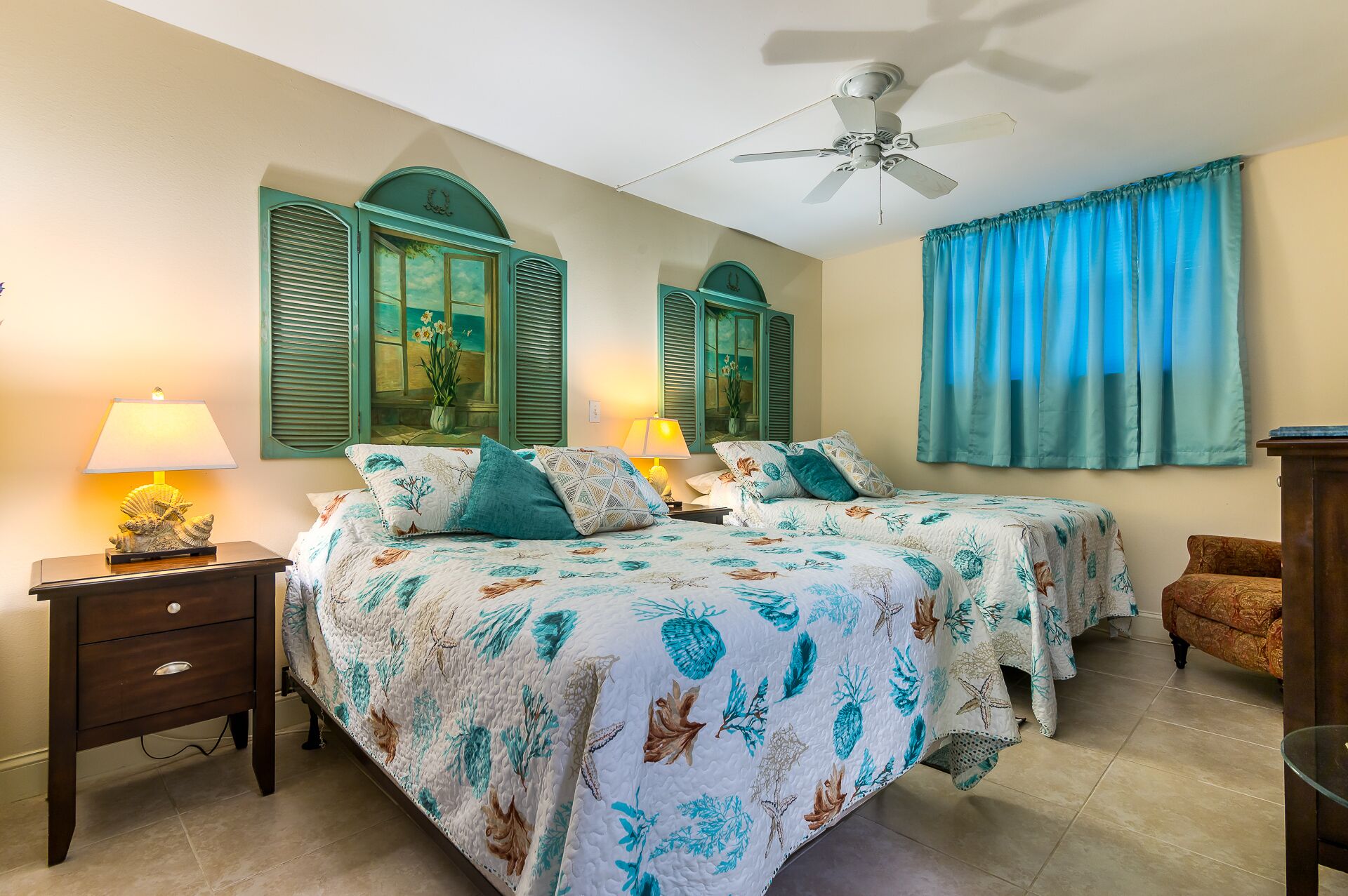 A bedroom with two beds, a ceiling fan, a nightstand with a lamp, and a dresser.
