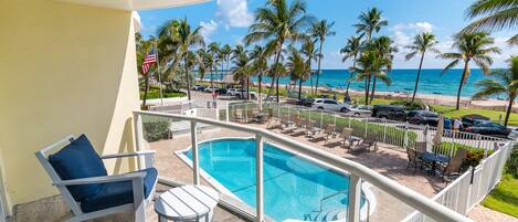 A balcony with a pool, lounge chairs, and a view of the beach and ocean.