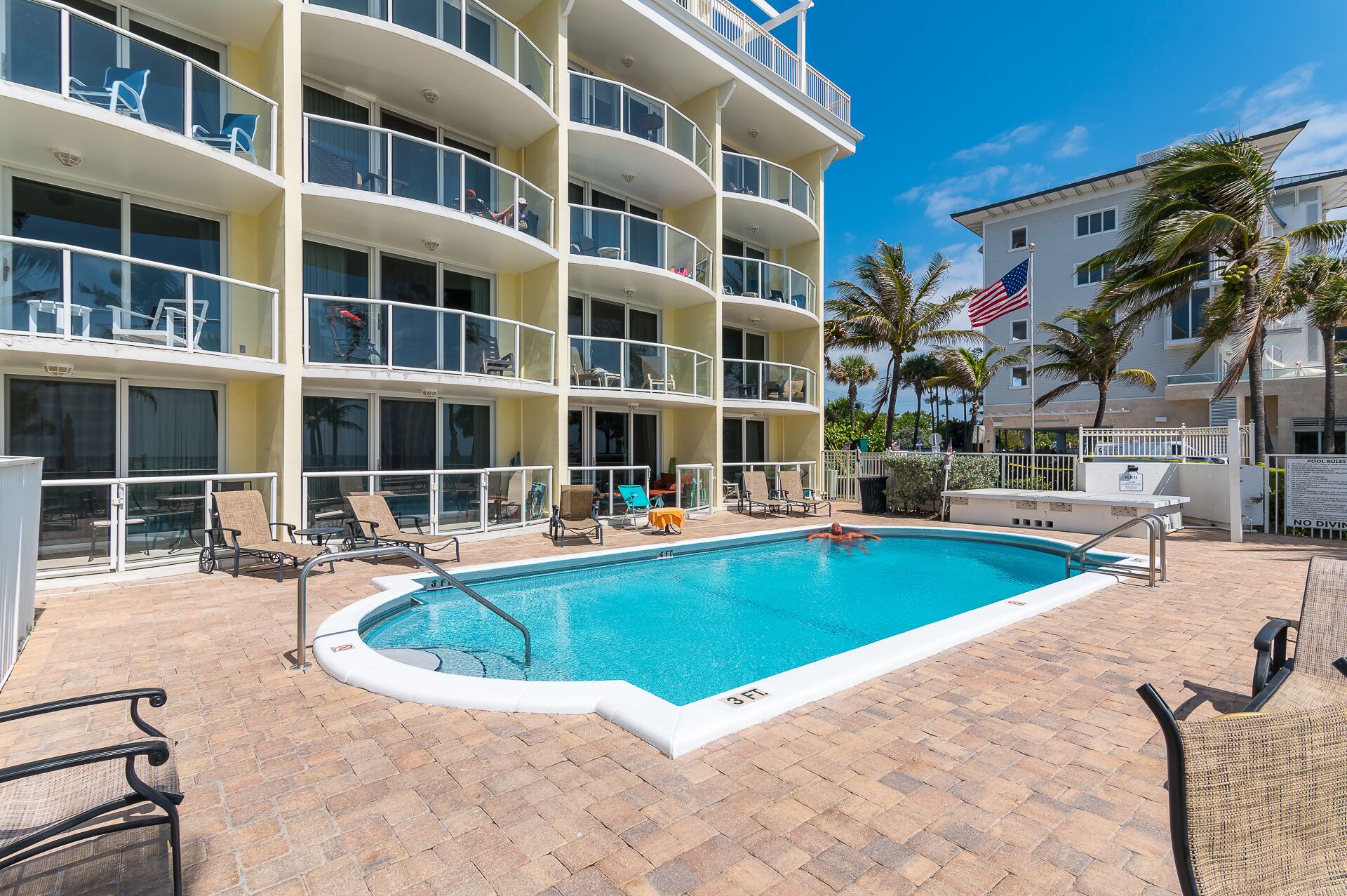 A multi-story hotel with a swimming pool, outdoor seating, and palm trees.