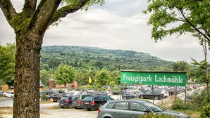 Un área de estacionamiento con un cartel que dice "Freizeitpark Lochmühle" y un paisaje montañoso de fondo.