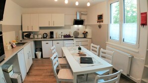Una cocina compacta con gabinetes blancos, una mesa de comedor con sillas, un horno empotrado y un ventanal con vistas a árboles.
