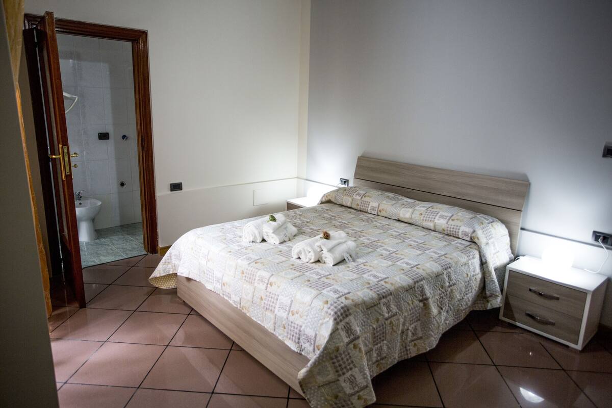 A bedroom with a bed, bedside tables, and a bathroom visible through an open door.