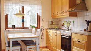 Eine Küche mit Holzausstattung, einem Bosch-Ofen, einem Fenster mit Vorhängen und einem Essbereich mit Tisch und Stühlen.