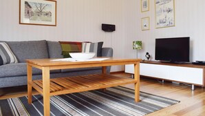 Ein modernes Wohnzimmer mit grauem Sofa, Couchtisch aus Holz, Flachbildfernseher und gerahmten Kunstwerken an der Wand.