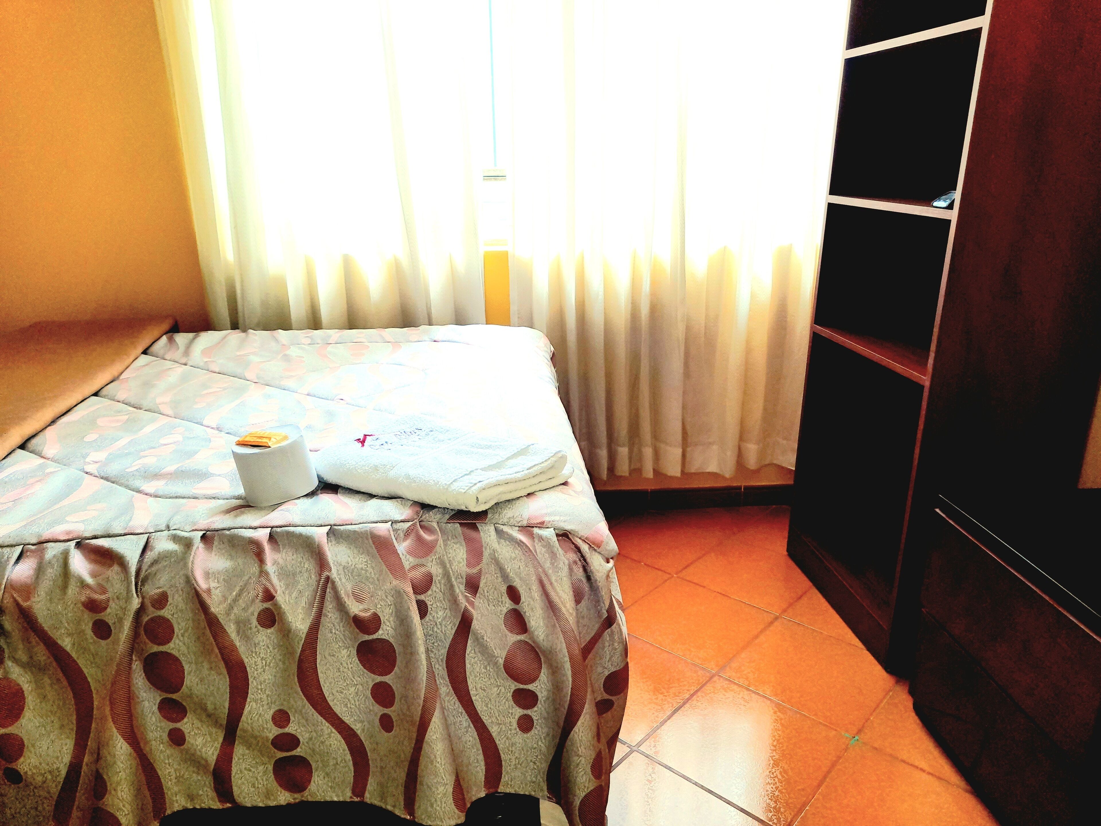 Una cama bien hecha con una colcha estampada, una almohada blanca y una toalla doblada.