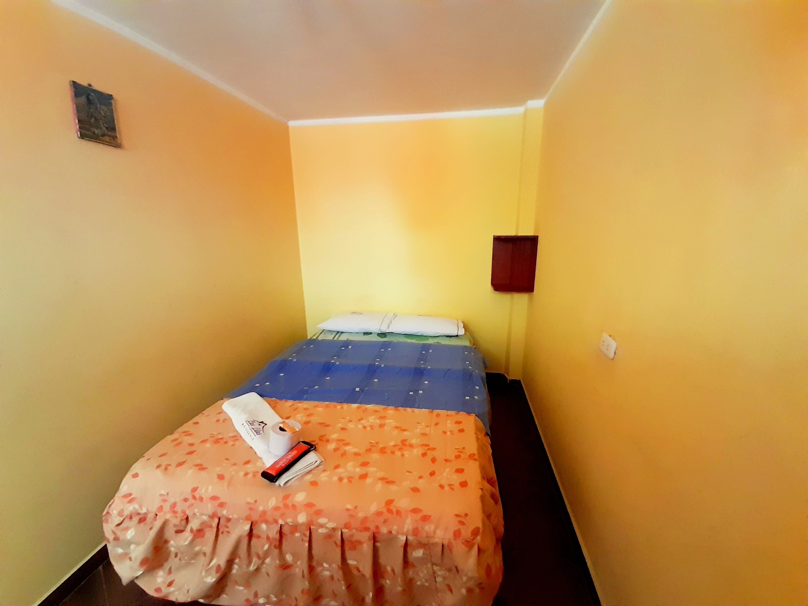 A small, narrow hotel room with a single bed, a nightstand, and a small table.