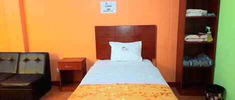 A hotel room with a bed, a nightstand, a wooden wardrobe, and a sofa.