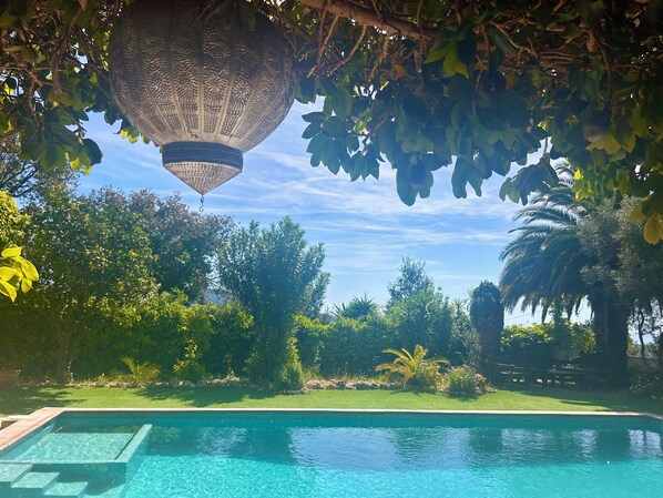 A swimming pool with a clear blue water surface, surrounded by lush greenery and a decorative hanging lantern.