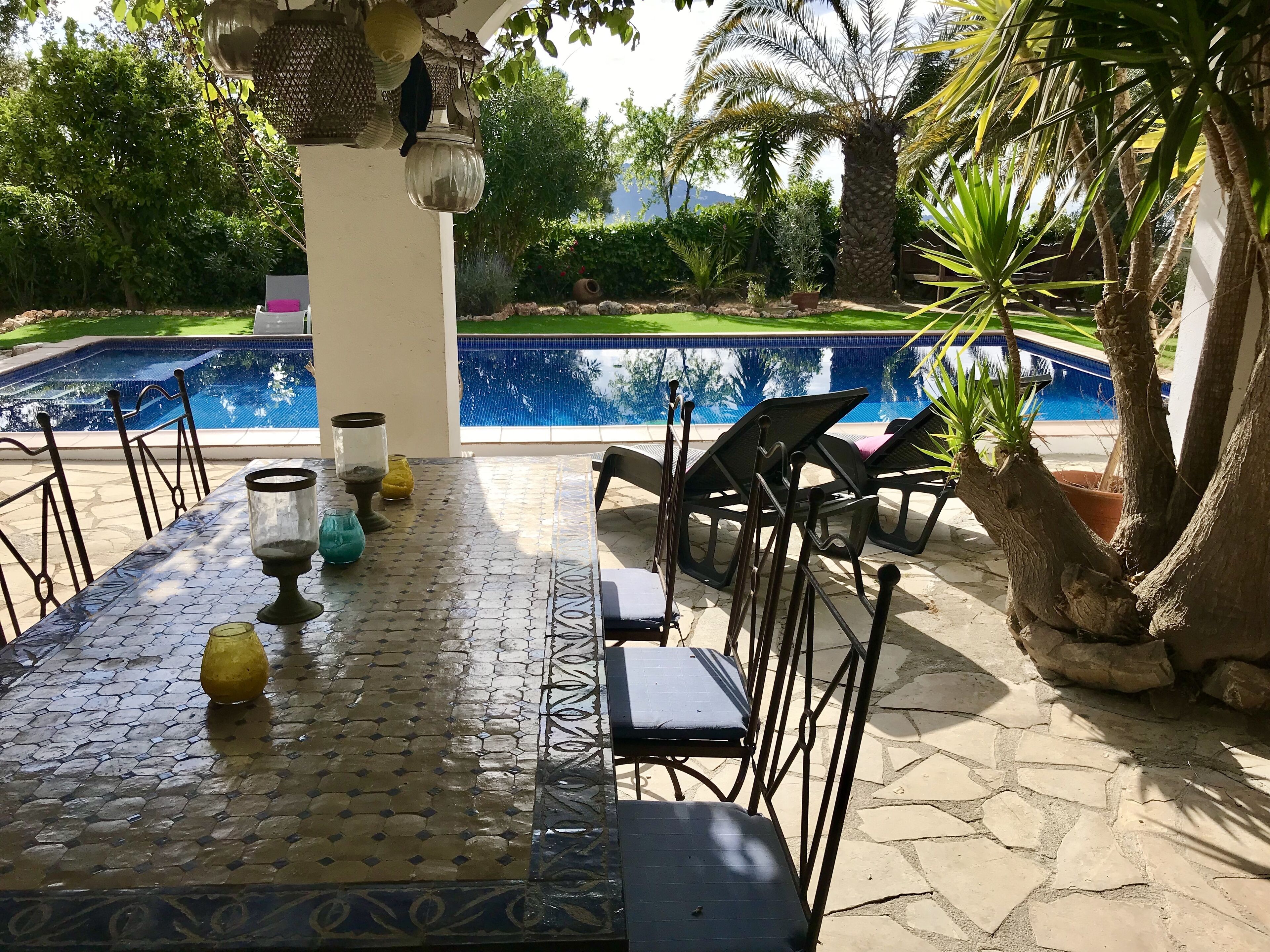 An outdoor patio with a pool, stone flooring, and a table set for dining.
