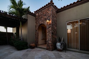 A stone archway leading to a covered patio area with a pergola, potted plants, and a large window. - Paraiso Del Mar Resort V58 4 Bed by Casago (La Paz)