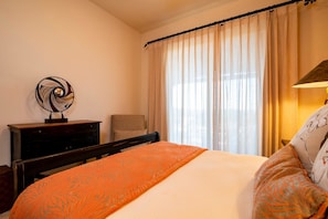 A neatly arranged hotel room with a bed, a nightstand, a lamp, and a window with curtains. - Paraiso Del Mar Resort V58 4 Bed by Casago (La Paz)