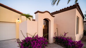 A residential house with a garage, a small porch, and vibrant purple bougainvillea plants. - Paraiso Del Mar Resort V1 3 Bed by Casago (La Paz)
