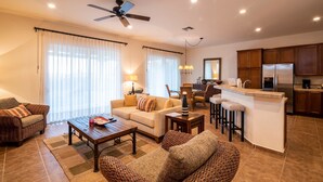 A spacious living area with a sofa, armchairs, a coffee table, and a kitchen area with a bar and stools. - Paraiso Del Mar Resort V1 3 Bed by Casago (La Paz)