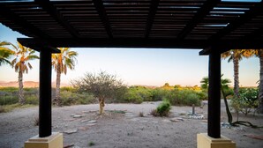 A covered outdoor area with a view of a desert landscape, palm trees, and a clear sky. - Paraiso Del Mar Resort V1 3 Bed by Casago (La Paz)
