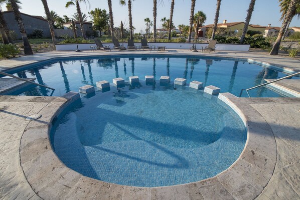 A round swimming pool with a tiled edge, surrounded by lounge chairs and palm trees. - Paraiso Del Mar Resort V103 3 Bed by Casago (La Paz)