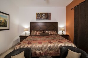 A bedroom with a bed, two bedside tables with lamps, a framed picture on the wall, and a dark curtain. - Paraiso Del Mar Resort B404 1 Bed by Casago (La Paz)