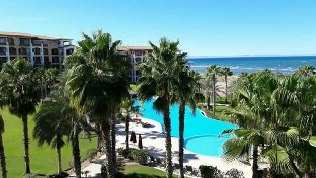 Un resort con una piscina grande rodeada de palmeras y vistas a la playa.