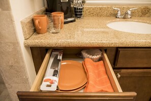 A kitchen counter with a coffee maker, a sink, and a drawer containing a knife, plates, and a towel. - Paraiso Del Mar Resort B404 1 Bed by Casago (La Paz)