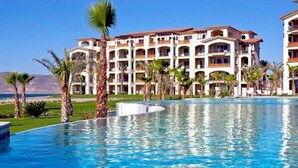 Un resort con una piscina grande, palmeras y un edificio de varios pisos con balcones.