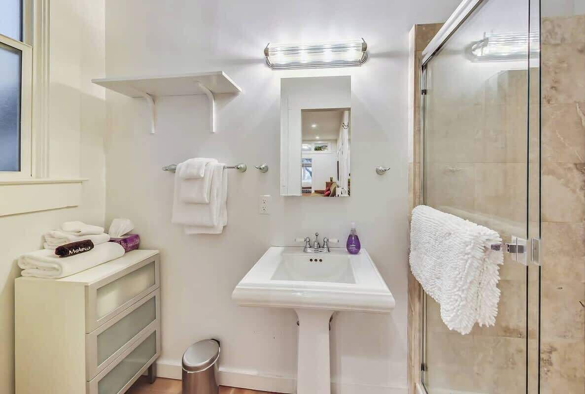 A bathroom with a white sink, a glass shower enclosure, a mirror, and a towel rack.