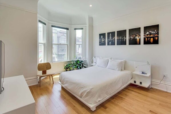 A bedroom with a large bed, a bedside table, a chair, and a window with a view of buildings.
