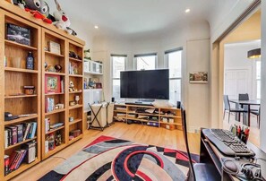 A living room with a TV, wooden bookshelves, a desk with a computer, and a large rug.