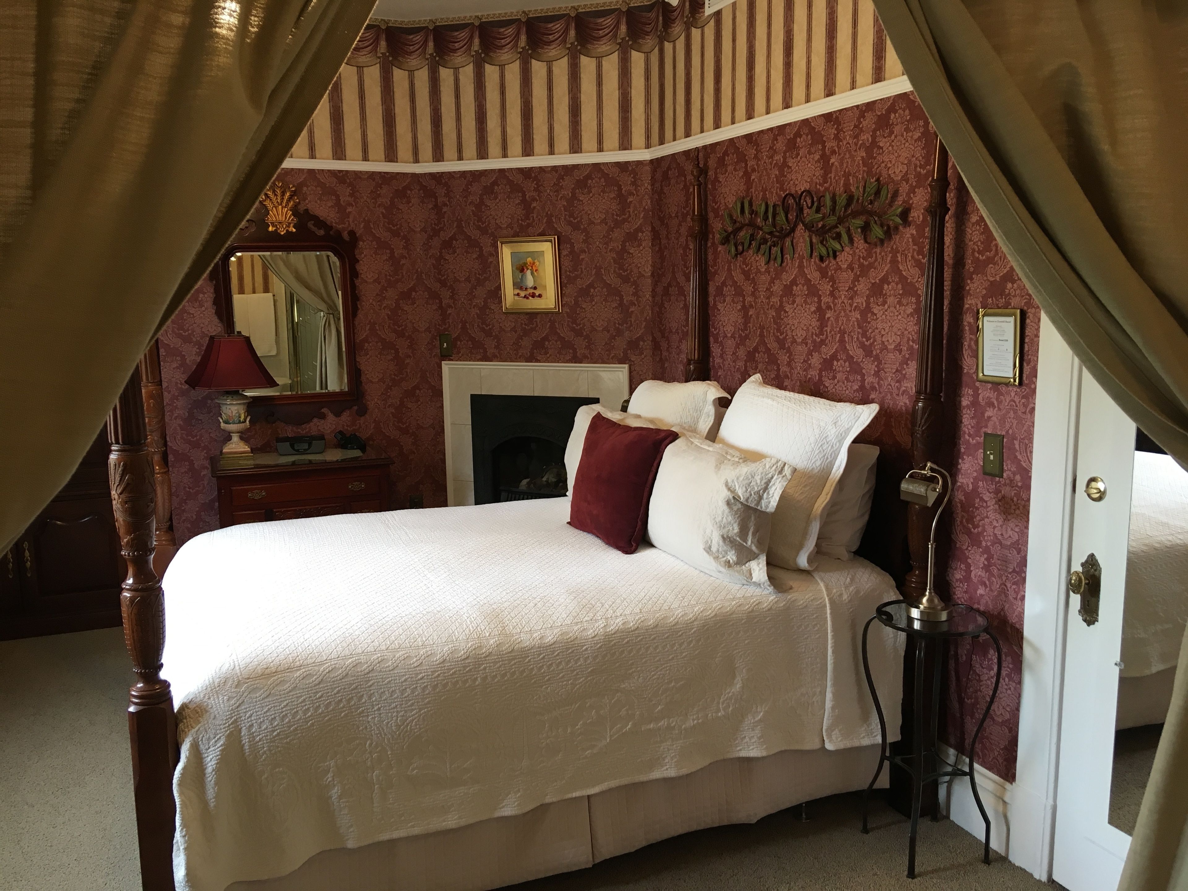 A bedroom with a large bed, a mirror, a fireplace, and a door.