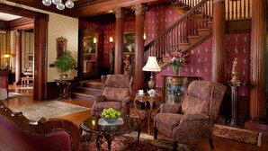A grand lobby with ornate wooden columns, a staircase, and patterned wallpaper. - Churchill Manor B&B (Napa)