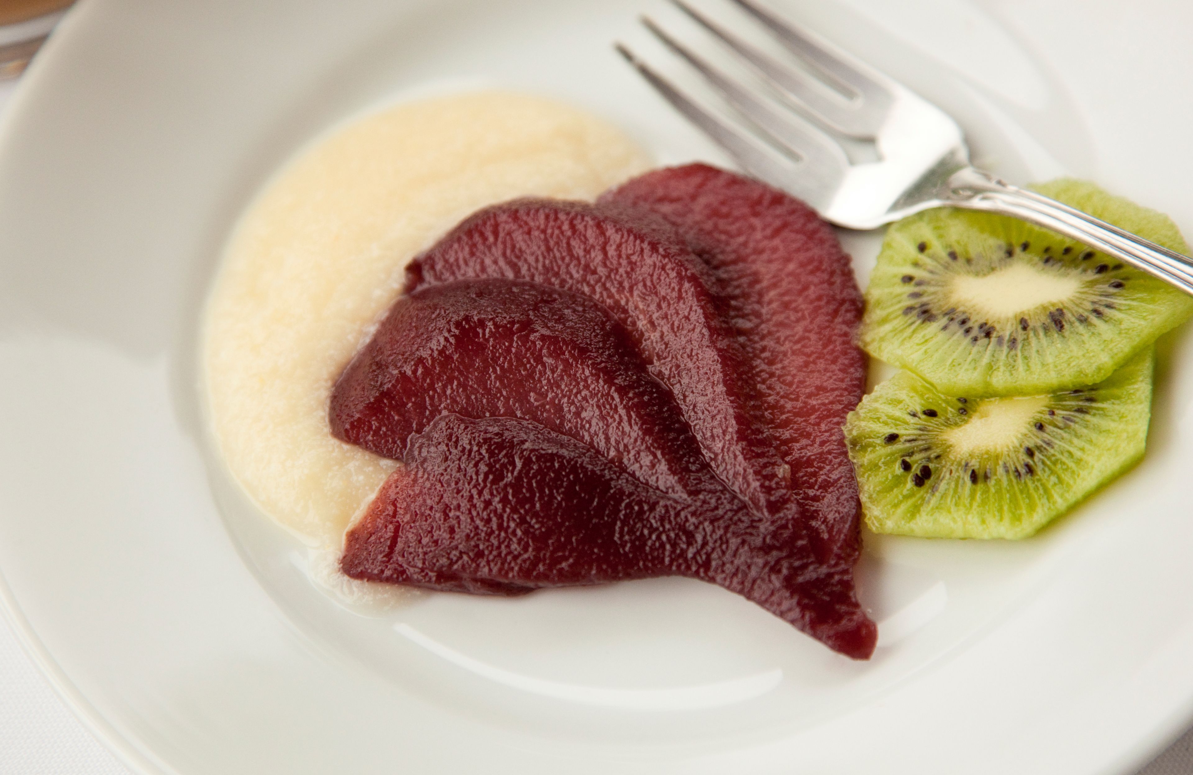 Un piatto con fette di barbabietola, un kiwi e una porzione di quello che sembra essere polenta.