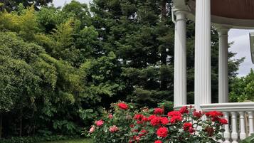 Un jardin agrémenté d’un belvédère blanc, d’une végétation luxuriante et de roses rouges.