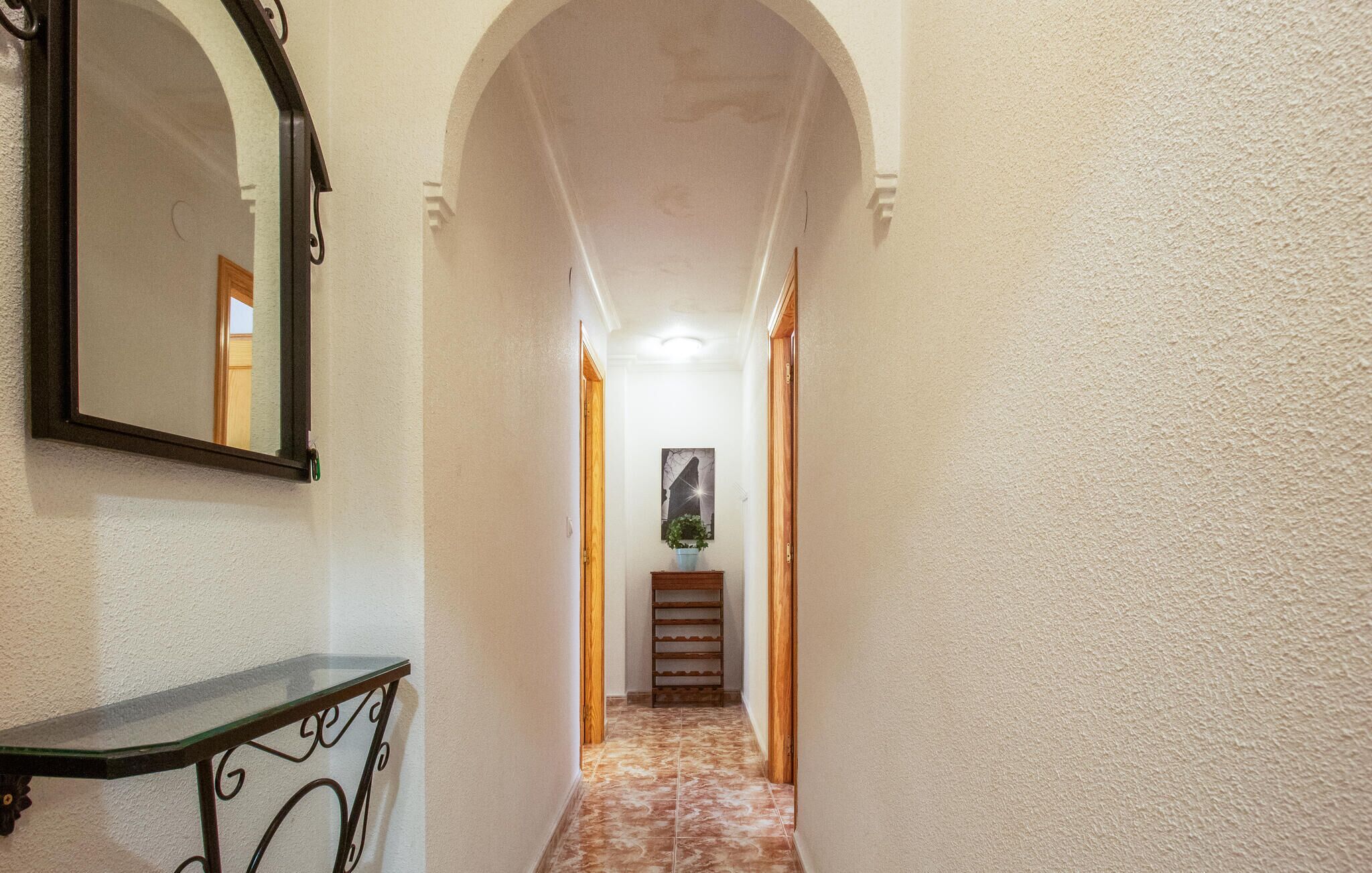 Un couloir avec un miroir, une petite table et un escalier menant à une autre pièce.