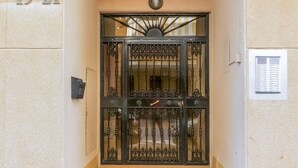 Un portail en métal noir orné de motifs complexes, une plaque numérotée indiquant les numéros « 19-21 », et une petite enseigne avec du texte, fixée au mur à côté.