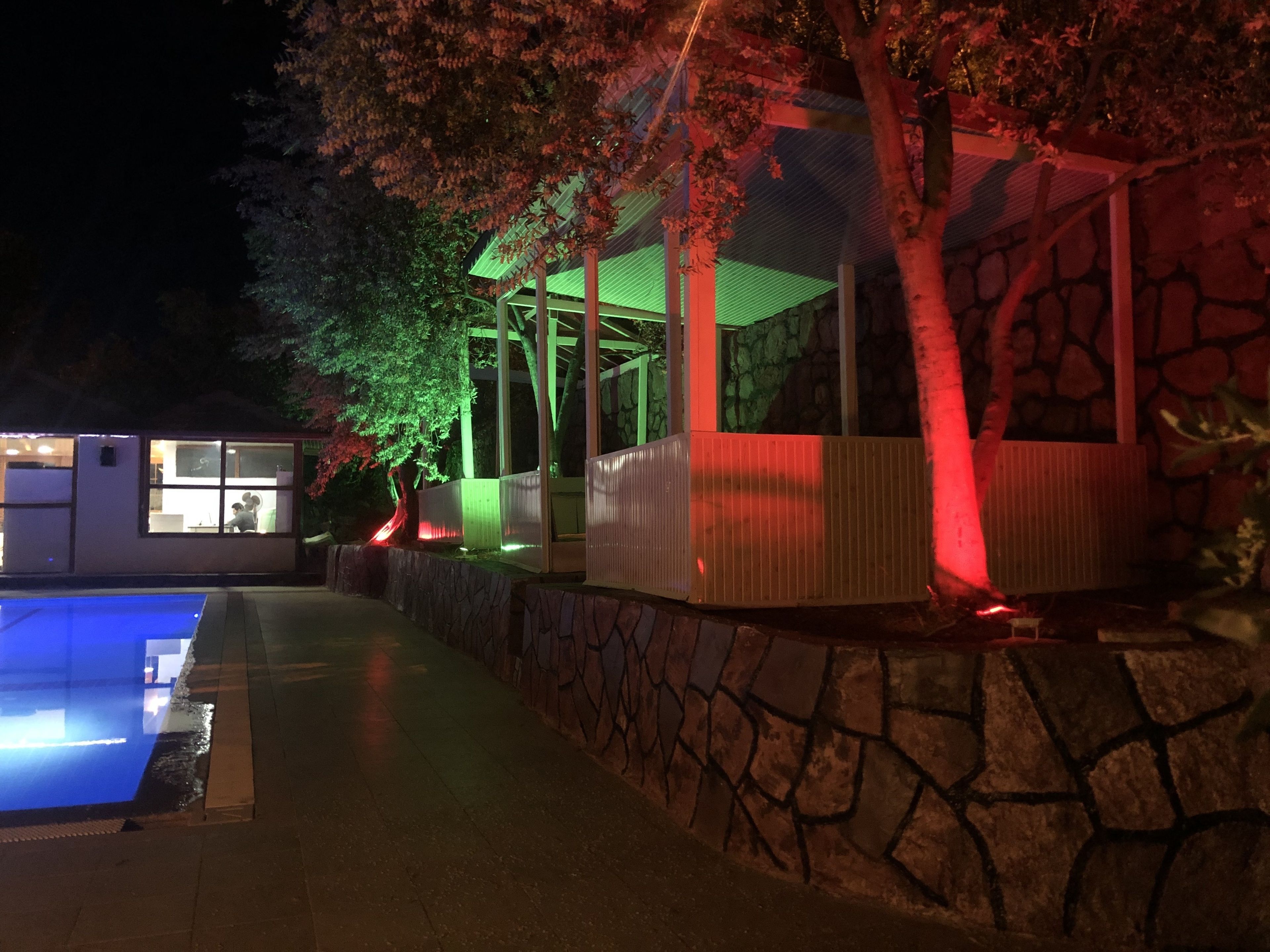 A poolside area with a stone wall, a covered seating area, and a building with windows.