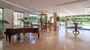 Eine geräumige Lobby mit einem Flügel, bequemen Sitzgelegenheiten und großen Fenstern mit Blick ins Freie.
