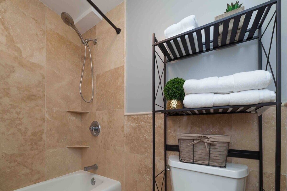 A bathroom with a bathtub, a shower, and a shelf with towels and toiletries.